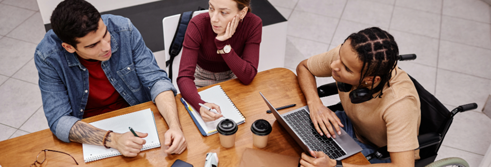 Three people working together around a table with a laptop and notebooks.