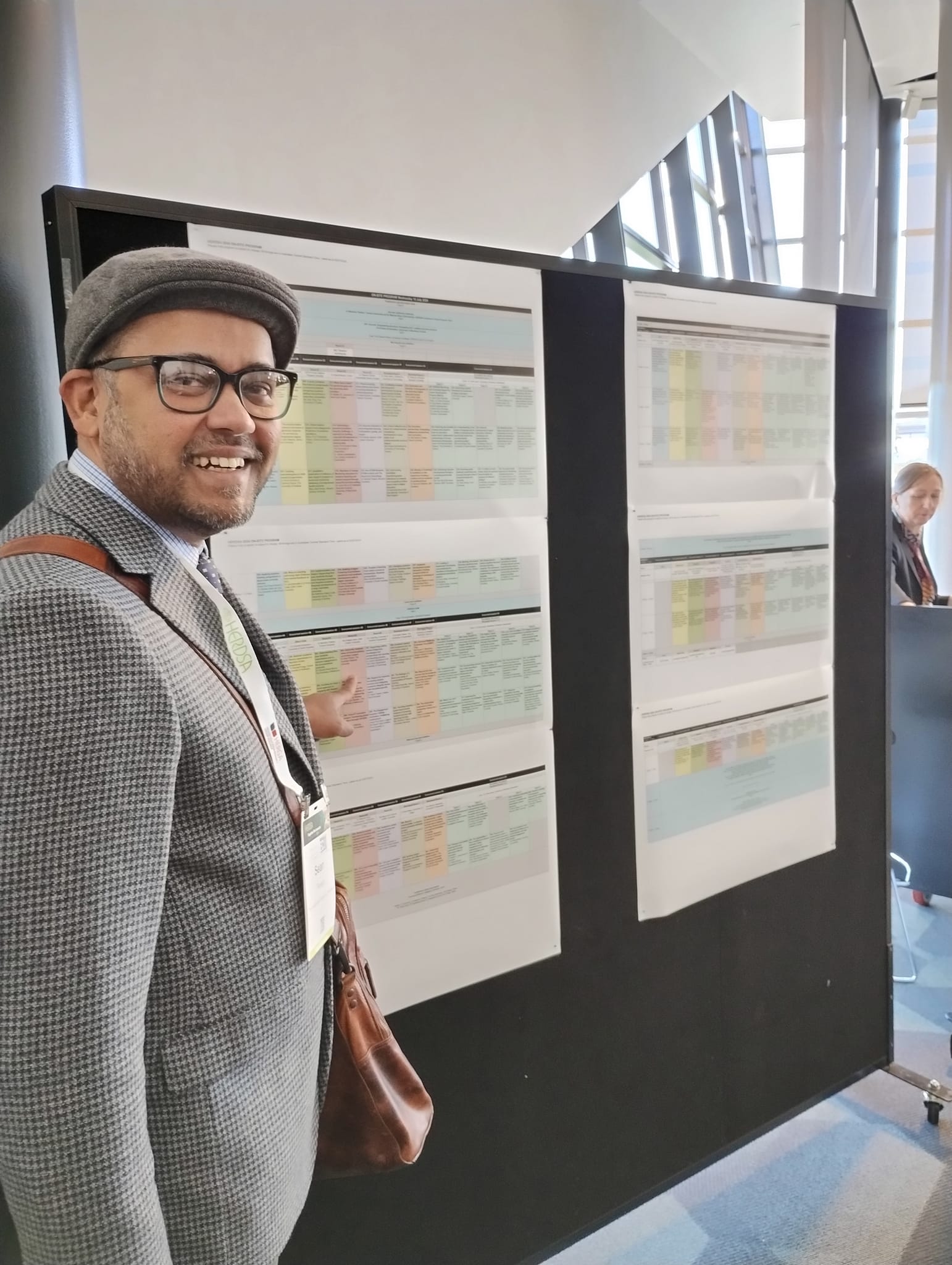 Sean Perera standing in front of the HERDSA conference program, pointing at his presentation